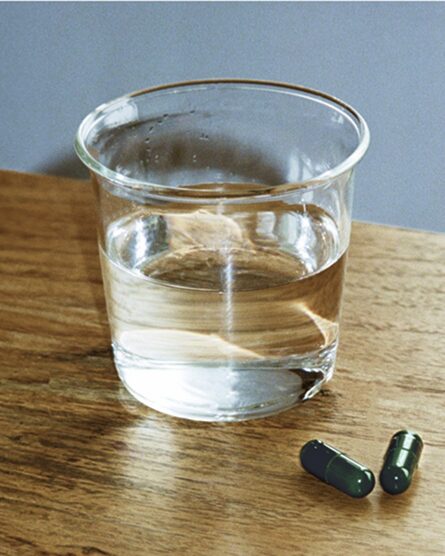 A glass of water with two Akka capsules next to it.